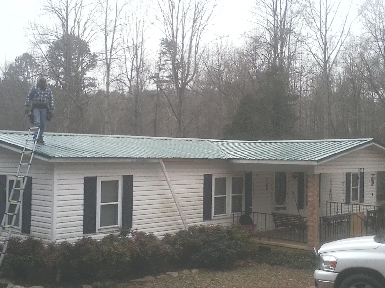 Worker on a ladder beside a new green metal roof on a ranch home in Bronson