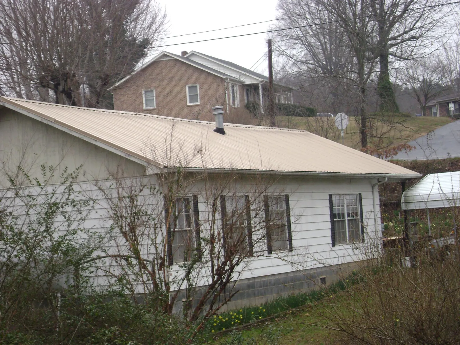 Tan metal roof on a white sided house set into a hillside — Commercial Roofing by Roofing Brothers in Bronson