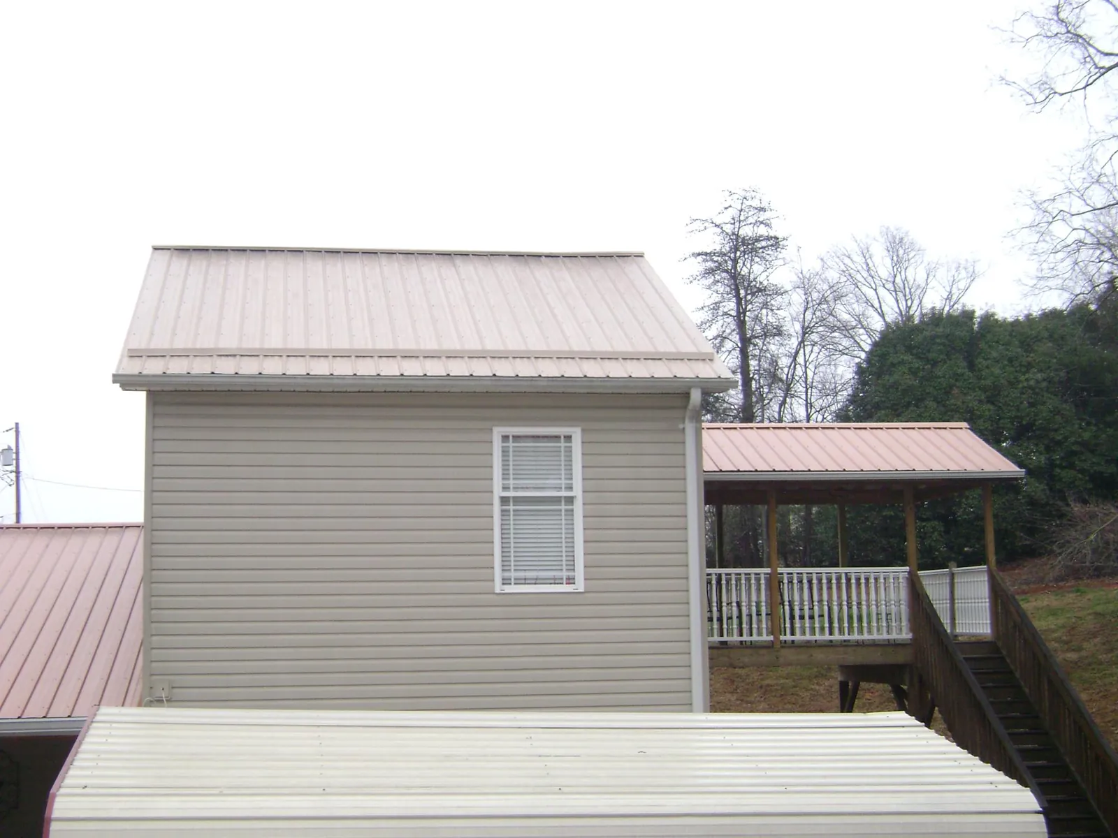 Tan metal roofs on a two story addition and attached porch, from a Roof Replacement job in Bronson